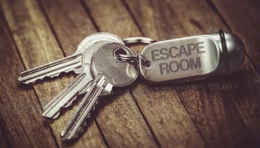 3-4 keys on a wooden table coonected to the chain with the text "escape room"